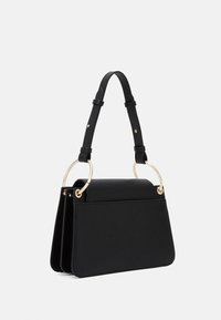 Musta nahkainen käsilaukku, jossa on suorakaiteen muotoinen muotoilu, kultasävyiset pyöreät metalliosat, kaksi olkahihnaa ja sileä pinta. Etupuolella on litteä muotoilu.