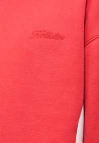 Sweatshirt rosso con logo "Hollister" ricamato, realizzato in morbido tessuto misto cotone, con una superficie liscia e una vestibilità comoda.