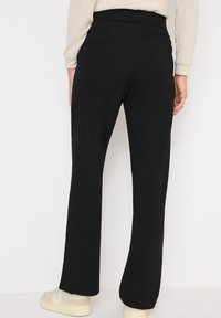 Svarta vida byxor med elastisk midja, slät textur, två bakfickor, kombinerade med beiga sneakers. Lämpliga för avslappnad stil.