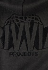 Crni pamučni materijal sadrži istaknuti, izbočeni tekst "RIVW" i "PROJECTS", s teksturiranim dizajnom i mat završetkom.