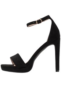 Svart mocka högklackad sandal med ankelrem. Har ett brett framband och en plattformsula för ökad höjd och stabilitet.