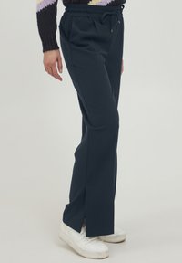 Marineblauwe broek met een ontspannen pasvorm, elastische tailleband met trekkoord, zijsplitsen en gecombineerd met witte sneakers.