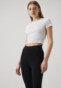 White ribbed cropped t-shirt with short sleeves, paired with high-waisted black leggings. Smooth texture, minimal design, and no patterns.
