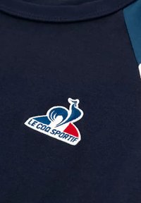 Camicia in cotone blu navy con logo ricamato "Le Coq Sportif" in bianco, rosso e blu, con una texture liscia e design classico a girocollo.