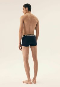 Granatowe bawełniane slipy z szerokim czarnym i złotym, markowym paskiem, prezentujące gładką teksturę i dopasowany krój na plecach modela.