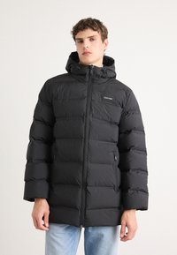 Zwarte donsjacket met capuchon, voorzien van een ritssluiting aan de voorkant, een gewatteerd ontwerp en een logo op de borst. Glad, waterafstotend materiaal.