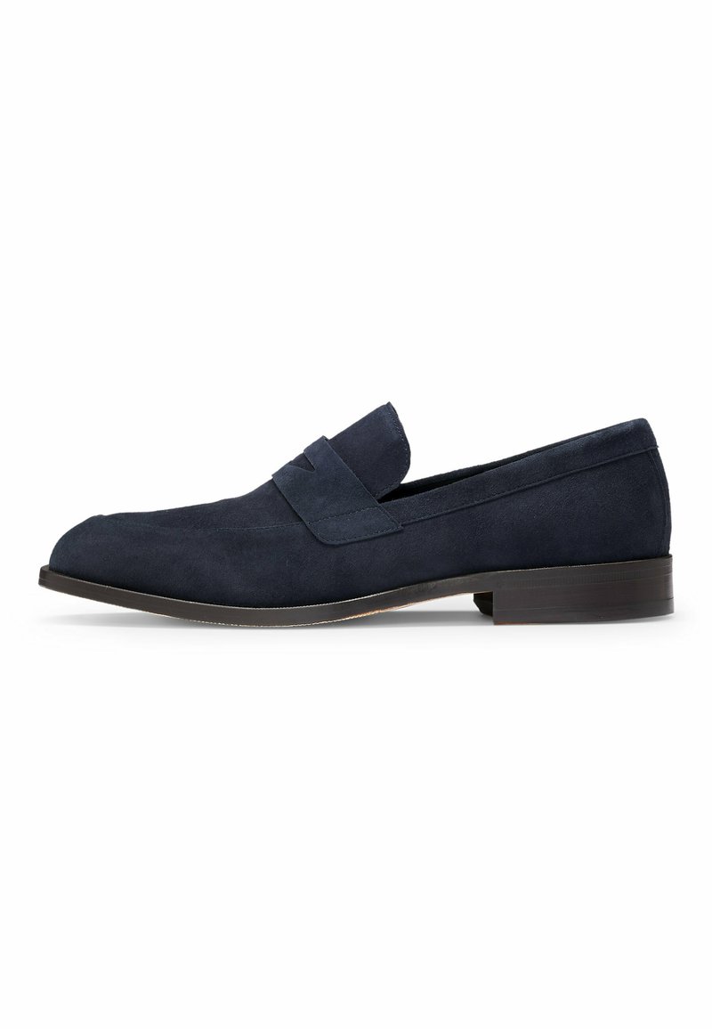 Mocassins en daim bleu marine avec un talon plat, présentant une texture lisse et une sangle sur le dessus. Design simple et épuré.