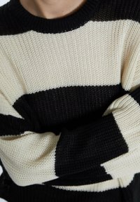 Maglione lavorato a maglia con strisce orizzontali nere e crema, collo a girocollo a coste e una finitura testurizzata. Le maniche sono arrotolate ai polsini.