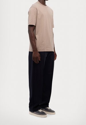 Camiseta de manga corta beige de algodón, combinada con pantalones sueltos azul marino y zapatillas grises, mostrando un ajuste relajado y una textura suave.