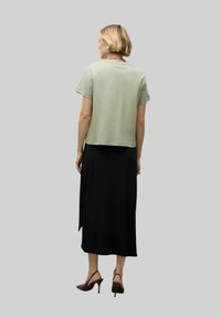 Lysegrøn bluse med korte ærmer, kombineret med en sort ankel-lang nederdel. Outfittet har en afslappet pasform og en glat tekstur.