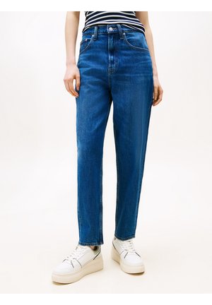 Personne portant un jean bleu taille haute avec des jambes droites, associé à un haut rayé noir et blanc et des baskets blanches à plateforme.
