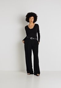 Črn dolg ročna majica z drapiranim izrezom, v kombinaciji z visokimi, ohlapnimi črnimi hlačami in ozkim črnim pasom z kovinsko sponko.