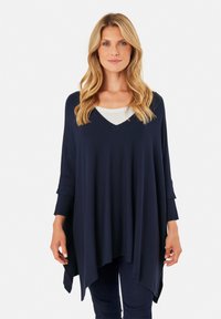 Tunique blu navy, con una vestibilità ampia, scollatura a V e maniche a tre quarti. Tessuto morbido e testurizzato con orlo curvo. Indossata sopra un top bianco.