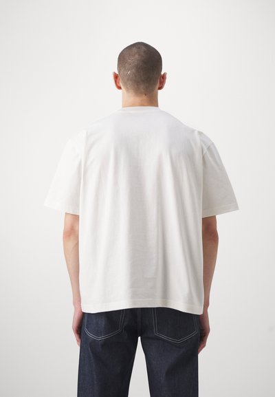 T-shirt en coton blanc avec des manches courtes, col rond, coupe décontractée et texture lisse. Porté avec un jean en denim foncé. Vue arrière simple.
