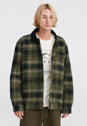 Grön och svart rutmönstrad skjortjacka med svart krage, med knäppning och två bröstfickor, bärs över en vit grafisk t-shirt.