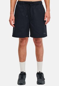 Shorts noirs à taille élastique avec cordon de serrage, design simple, poches latérales et un petit logo sur la jambe.