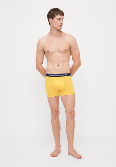 Żółte bawełniane bokserki z granatowym pasem, na którym widnieje logo "POLO RALPH LAUREN". Ubranie ma dopasowany krój i gładką teksturę.