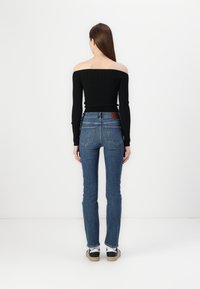 Black off-the-shoulder ribbed top paired with blue skinny jeans featuring back pockets and seam detailing, worn with black and white sneakers.