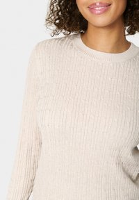 Beżowy sweter z prążkowanego materiału, z okrągłym dekoltem i długimi rękawami, z teksturowanym wzorem i lekkim wyglądem tkaniny.