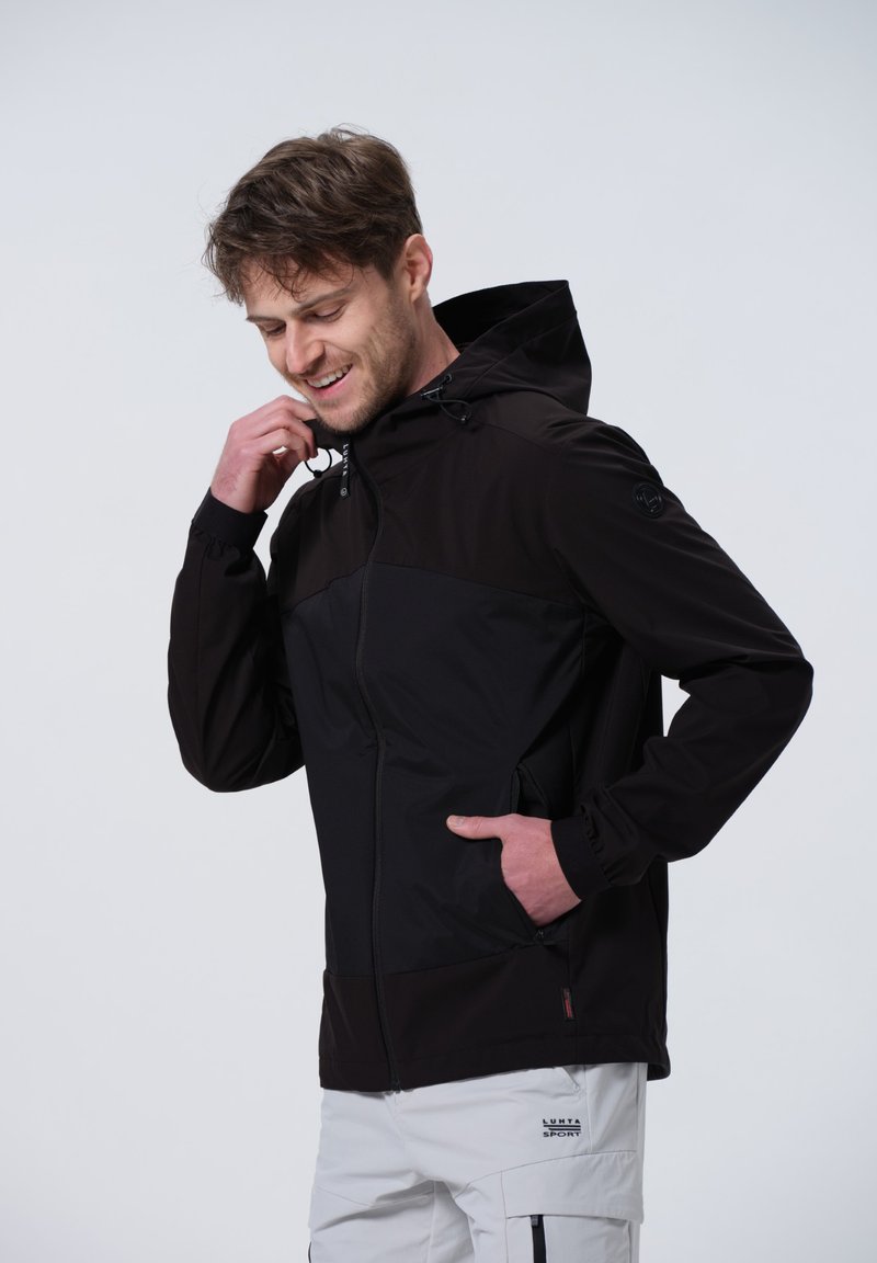 Chaqueta negra con cremallera y capucha, que presenta un diseño bicolor, puños elásticos y bolsillos con cremallera. Fabricada con material ligero y resistente al agua.