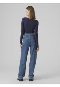 Navy langärmliges Oberteil und hochgeschnittene hellblaue Weitbeinjeans mit Gesäßtaschen und einem braunen Lederetikett am Bund. Schwarze Plateauboots.