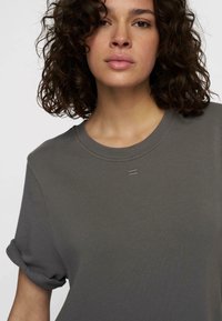 T-shirt court noir gris à manches courtes avec un col rond côtelé, des poignets roulés et un subtil détail cousu à l'avant. Texture de tissu douce.