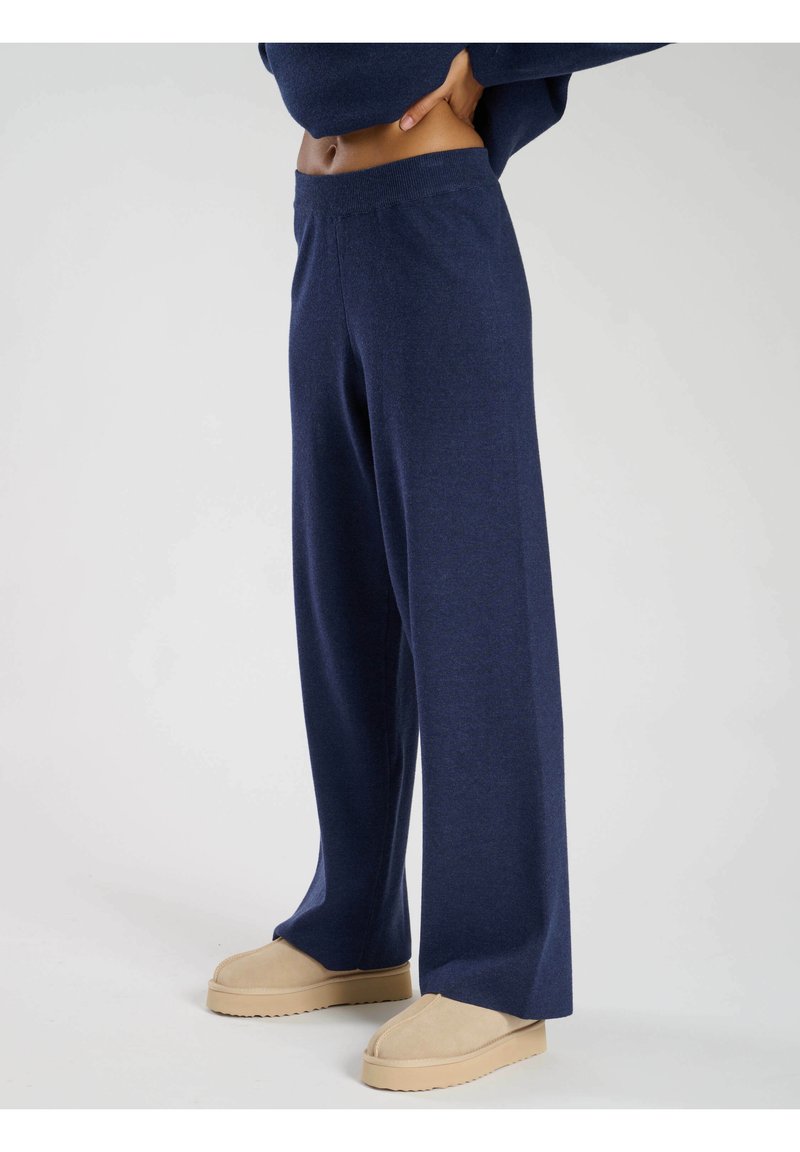 Pantaloni a gamba larga blu navy in un morbido tessuto con una texture liscia, dotati di una vita elastica e abbinati a pantofole beige.