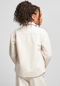 Licht beige, langemouwshirt met een kraag, zachte textuur en detail op de achterkant. Heeft zijzakken en een relaxte pasvorm.