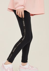 Melnas legingas ar sānu lentīti ar uzrakstu "BAKER by TED BAKER." Kombinētas ar baltām un rozā sporta kurpēm. Mīksts audums, pieguļošs dizains.