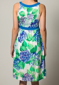 Kwiatowa sukienka z białym tłem w niebieskie i zielone wzory hortensji, dopasowanym wcięciem w talii oraz niebieskim wykończeniem dekoltu.