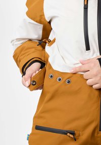 Brown and white ski jacket featuring a zippered pocket, snap closures, adjustable drawstring, and textured fabric for cold conditions.