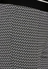 Svart och vit mönstrad tyg med ett geometriskt mönster. Har en solid svart midja. Slät textur med ett konsekvent mönster genom hela tyget.