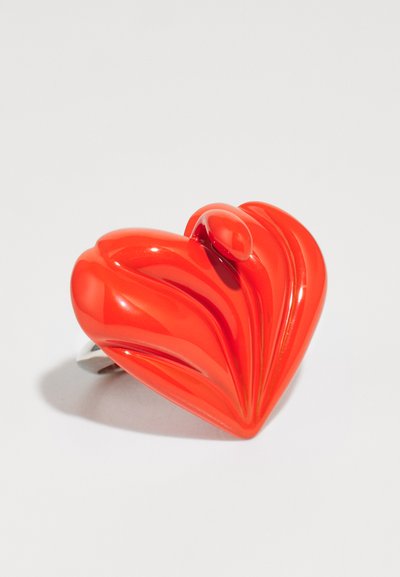 Bague rouge en forme de cœur avec une finition brillante, présentant des détails texturés ondulés et une bande en argent.