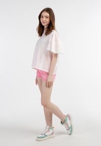 Top bianco con maniche corte a volant e pois rosa, abbinato a pantaloni corti rosa e sneakers alte multicolori con suola bianca.