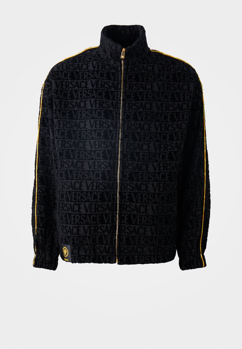 Schwarze Zip-Jacke aus strukturiertem Stoff mit einem Allover-Logo-Muster von Versace und gelben Streifen an den Seiten. Rundhalskragen.