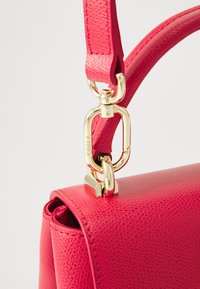Sac à main en cuir texturé rose avec des accessoires en or, doté d'une sangle robuste et d'un fermoir distinctif pour une fermeture sécurisée.