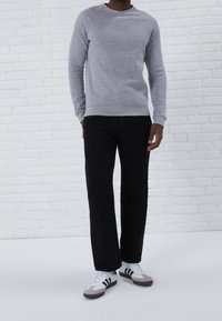 Sweatshirt gris clair avec col rond, poignets et ourlet côtelés ; associé à un pantalon noir à jambe droite et des baskets blanches avec des accents gris.
