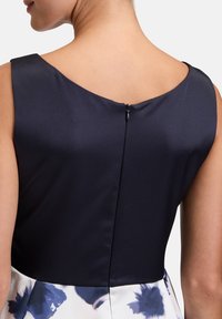 Marineblaues Kleid mit einem einfarbigen, glatten Oberteil und einem floral gemusterten Rock; verfügt über einen unauffälligen Reißverschluss auf der Rückseite für den Verschluss.