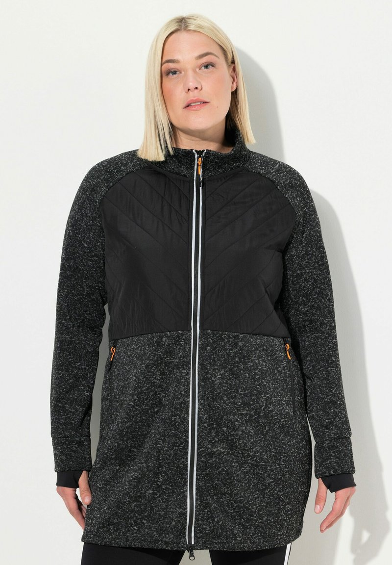 Schwarze und graue Mischgewebejacke mit gestepptem Vorderteil, Reißverschluss, Seitentaschen und kontrastierenden orangen Akzenten. Strukturiertes Strickmaterial an den Ärmeln.