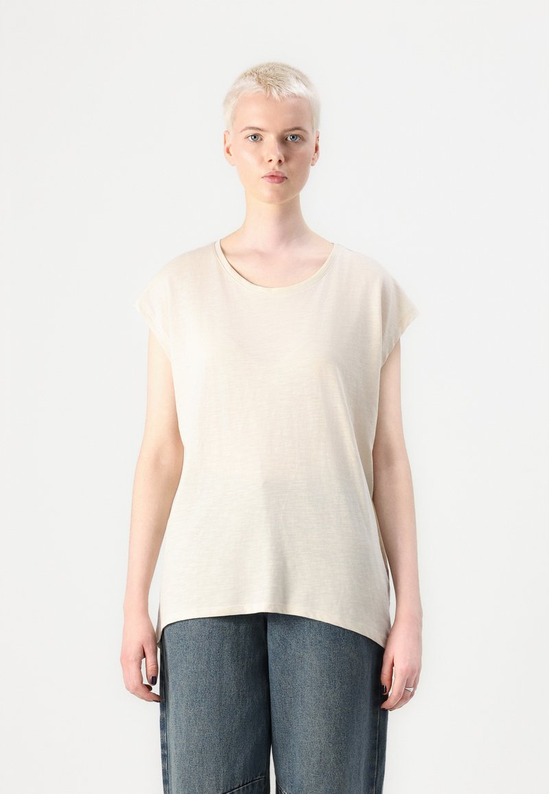 Beige, rövid ujjú póló, kerek nyakkal, puha, texturált anyagból készült. A póló lazán illeszkedik, magas derékú farmernadrággal párosítva.