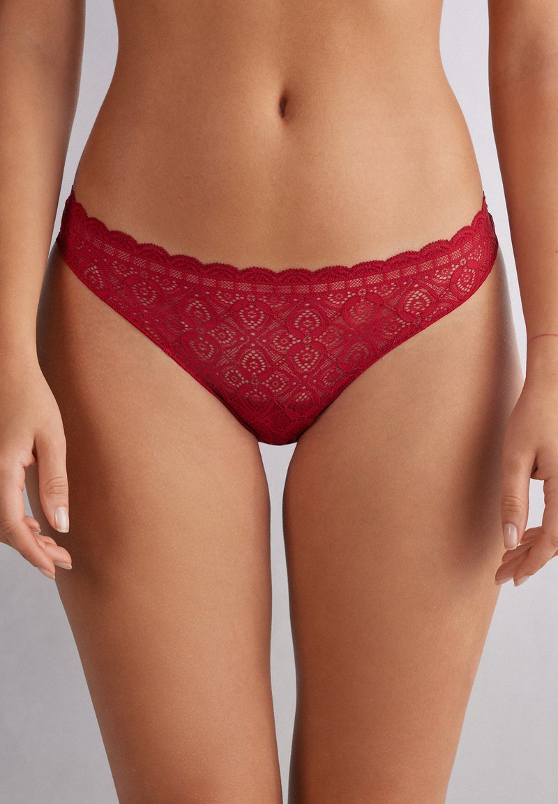 Red lace thong with scalloped edges, intricate floral pattern, and delicate trim. Soft, semi-sheer material with a low-rise design.