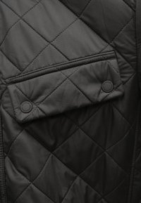 Czarna pikowana kurtka z kieszenią z patką z okrągłymi guzikami i kontrastowym przeszyciem, o gładkiej, matowej fakturze.