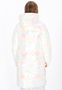 Fehér puffakabát, irizáló fényű, kapucnival és vízszintes tűzéssel. Simára puha textúra pasztell szivárványos kiegészítőkkel.