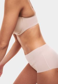 Bežová podprsenka a kalhotky s vysokým pasem, vyrobené z hladkého, elastického materiálu s bezešvým designem. Minimalistický styl bez viditelného šití nebo kovových prvků.