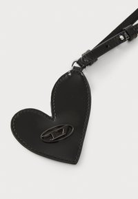 Black leather heart-shaped keychain with a glossy finish, featuring a metal logo accent and a small strap for attachment.