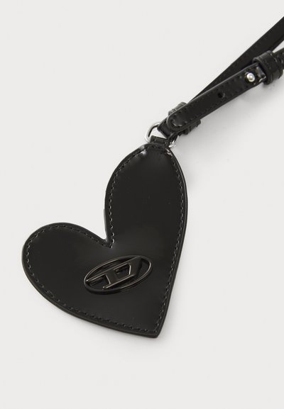 Porte-clés en cuir noir en forme de cœur avec une finition brillante, doté d'un accent en métal au logo et d'une petite sangle pour l'attacher.