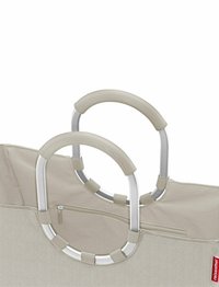 Bolso tote beige con tejido texturizado, asas dobles plateadas y un bolsillo con cremallera. Presenta un patrón de espiga y acentos de goma antideslizante.