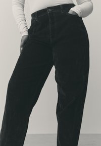 Sorte kordfløjlsbukser med høj talje og vide ben, der har forlommer, knaplukning og en blød, tekstureret stoffinish.