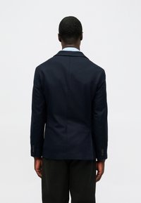 Blazer azul marino hecho de tela suave, con una única abertura, solapas muescas y dos botones en los puños. Diseño liso en la parte posterior.