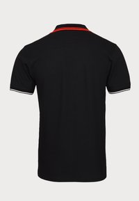 Le polo noir présente un design uni avec un col rouge et des accents rayés blancs sur les manches, fabriqué à partir d'un tissu en coton respirant.